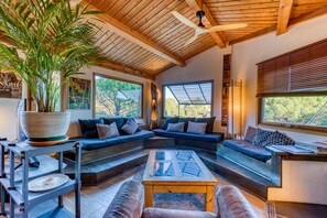 Un intérieur moderne avec un plafond en bois, de grandes fenêtres, un canapé d’angle et une plante en pot.