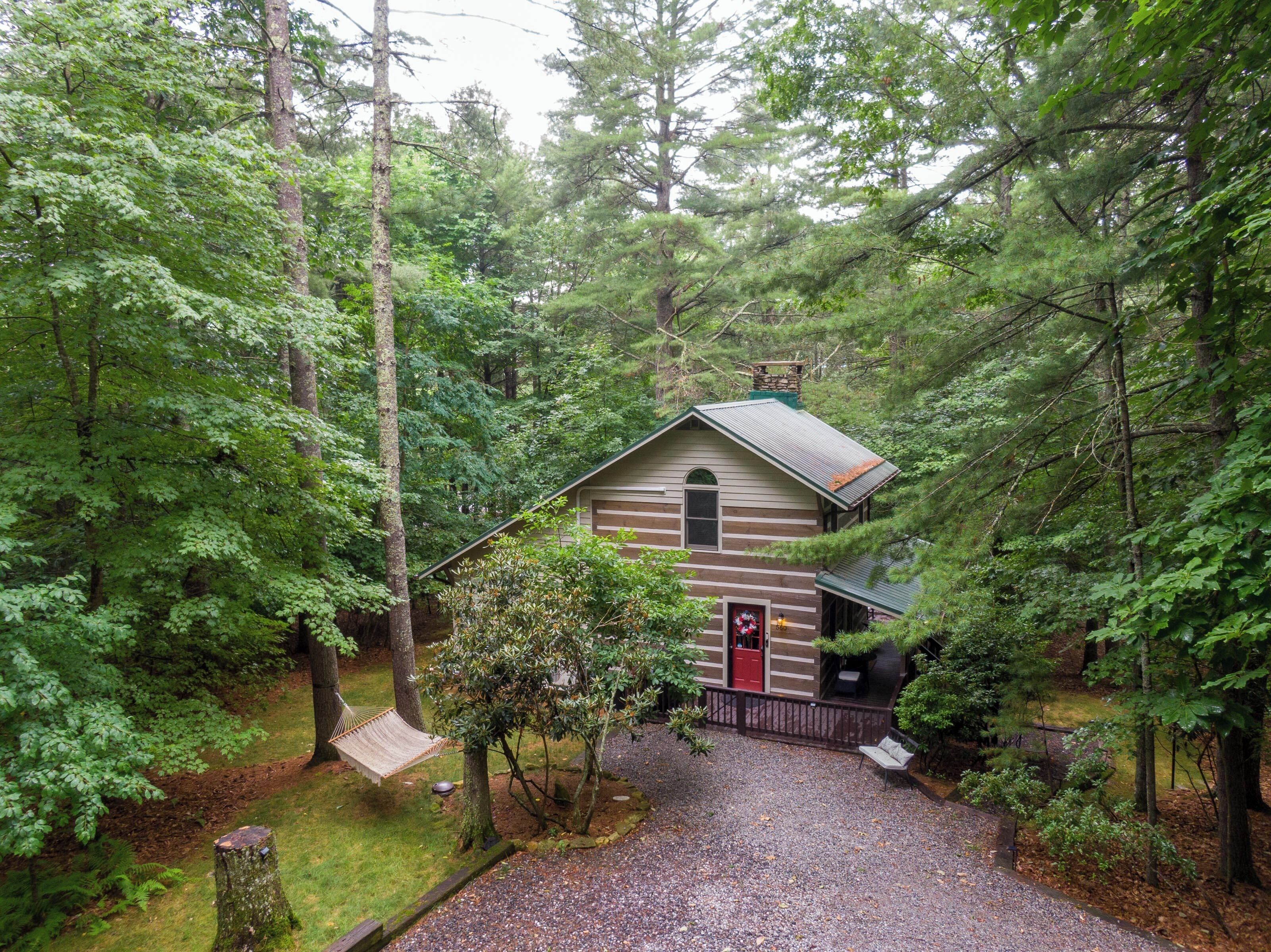 A cabin surrounded by dense forest, with a gravel driveway leading to the entrance.