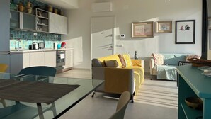 En moderne opholdsstue med et køkken, en gul sofa og et glasbord.