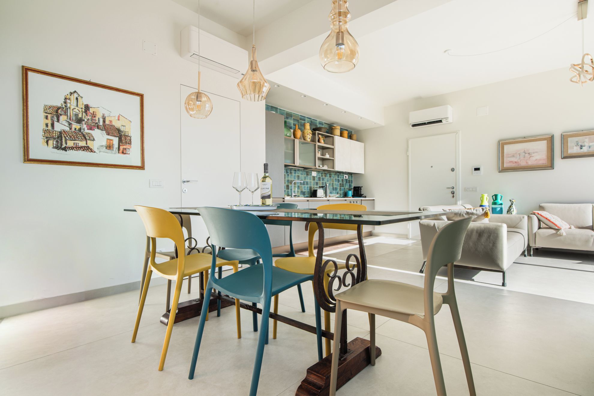 Una cucina moderna con mobili bianchi, un tavolo da pranzo con sedie colorate e luci a sospensione.