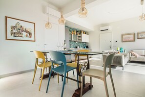A modern kitchen with white cabinets, a dining table with colorful chairs, and pendant lighting.