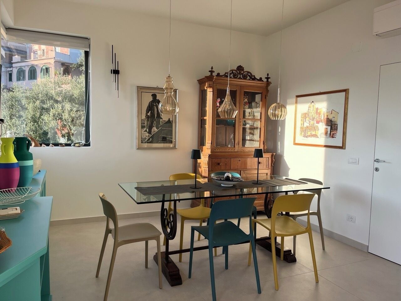 Un coin repas avec une table en verre, des chaises colorées et un buffet en bois.