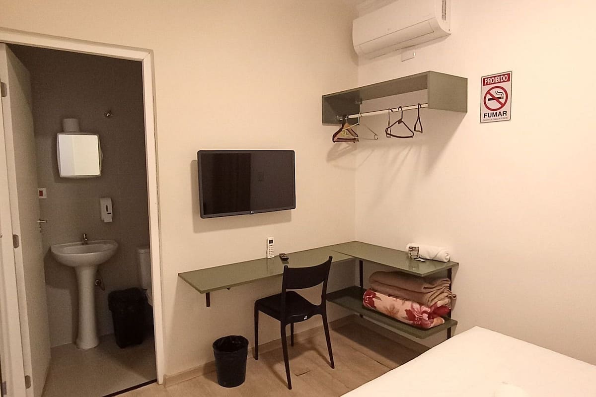 Ein Hotelzimmer mit Bett, Schreibtisch, Stuhl, Fernseher, Spüle und Mülleimer.