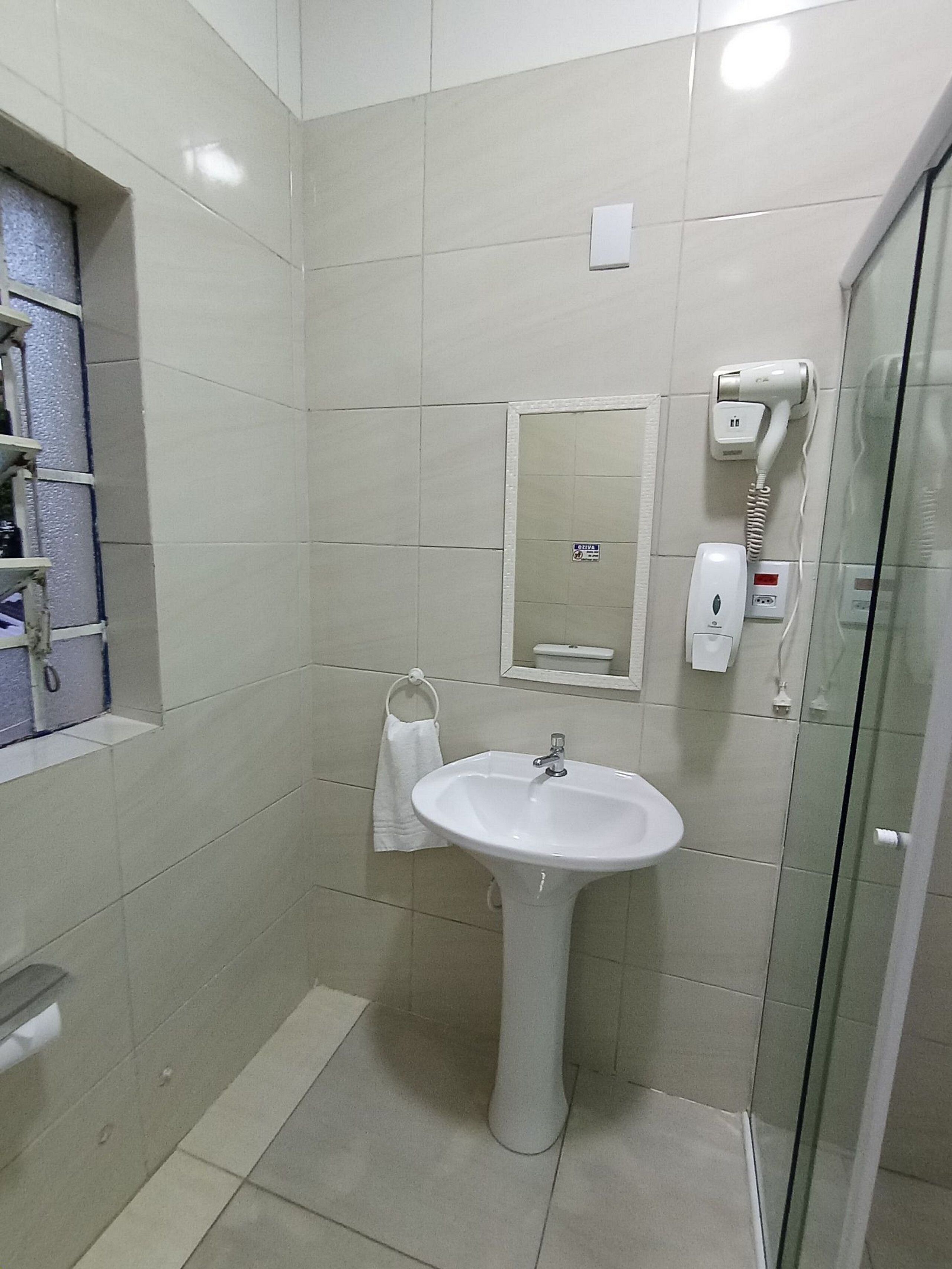 Une salle de bain avec un lavabo blanc, une cabine de douche en verre, un porte-serviettes et un sèche-cheveux fixé au mur.