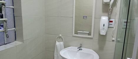 Une salle de bain avec un lavabo blanc, une cabine de douche en verre, un porte-serviettes et un sèche-cheveux fixé au mur.