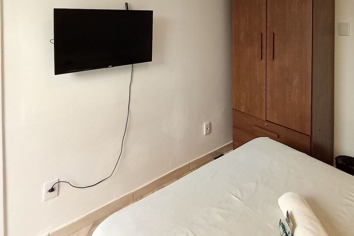 Ein Schlafzimmer mit einem Bett, einem an der Wand montierten Fernseher und einem Holzschrank.