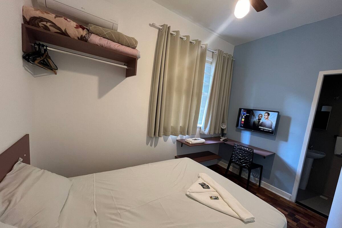 Ein Hotelzimmer mit Bett, Fernseher, Schreibtisch und einem Vorhangfenster.