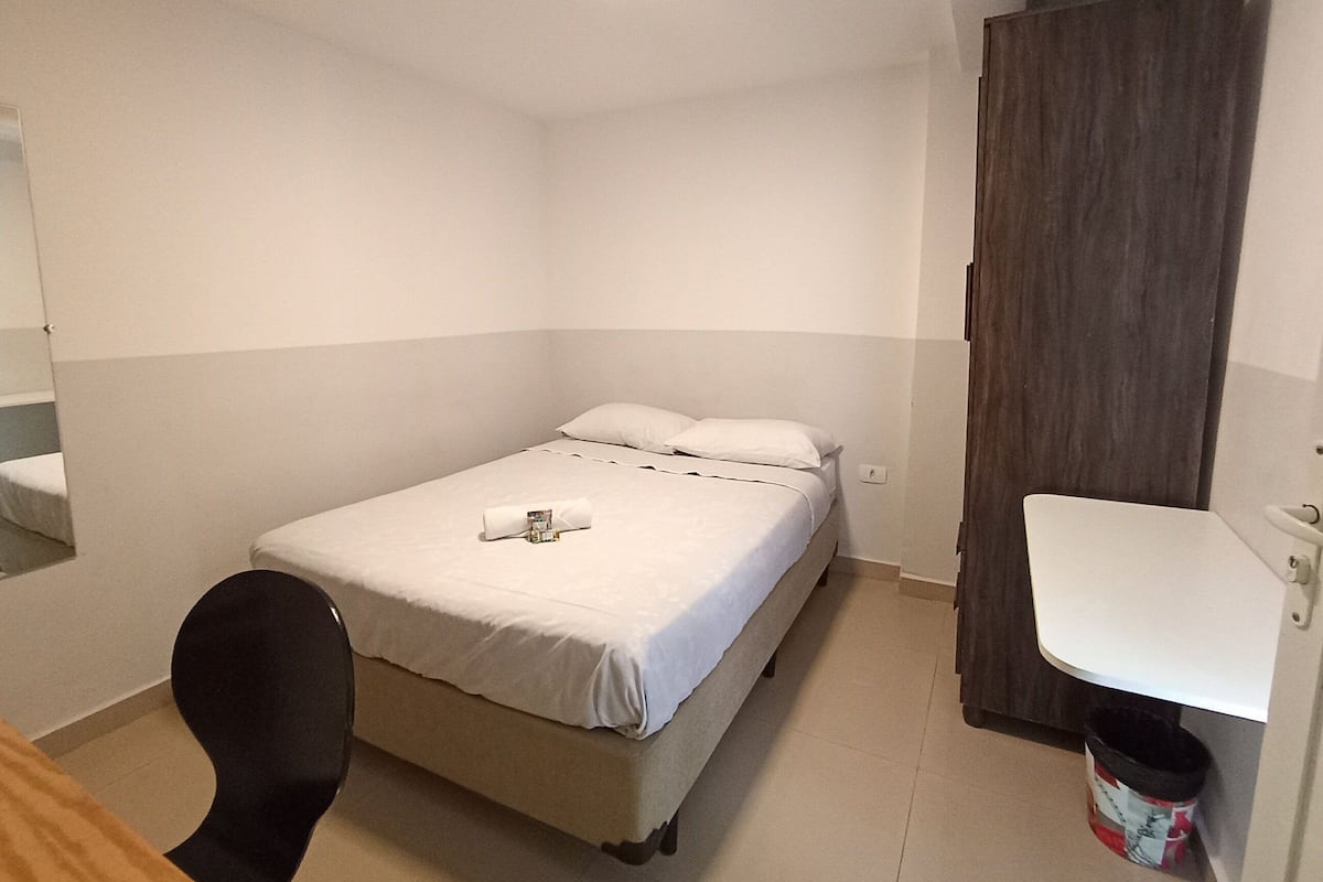 Ein kleines, sauberes Zimmer mit einem Bett, einem Sessel, einem Schreibtisch und einem Kleiderschrank.