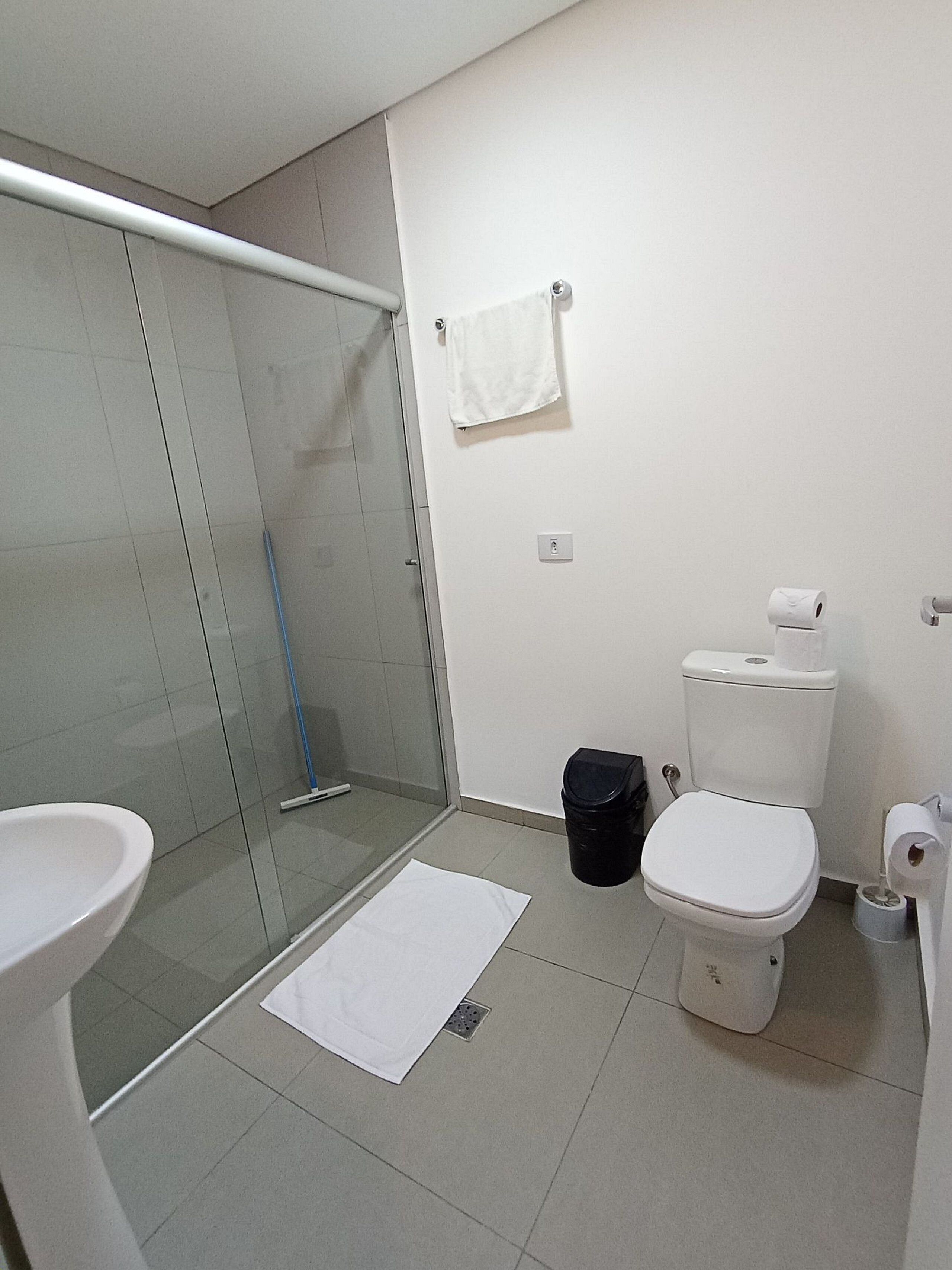 A bathroom with a glass shower enclosure, a toilet, a sink, and a trash bin.