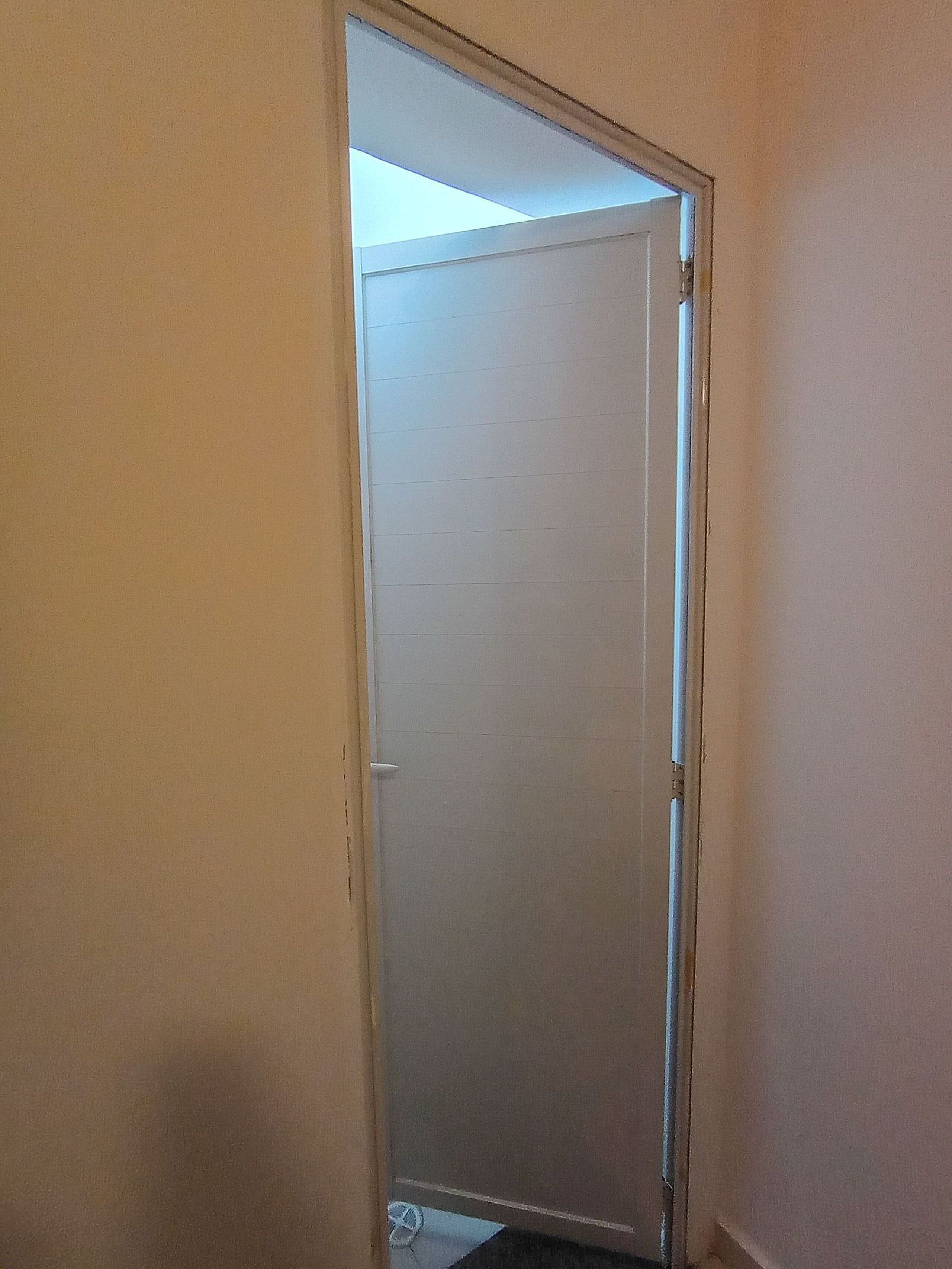 A narrow, white-framed door with a visible gap at the top, leading to a room with a tiled floor.