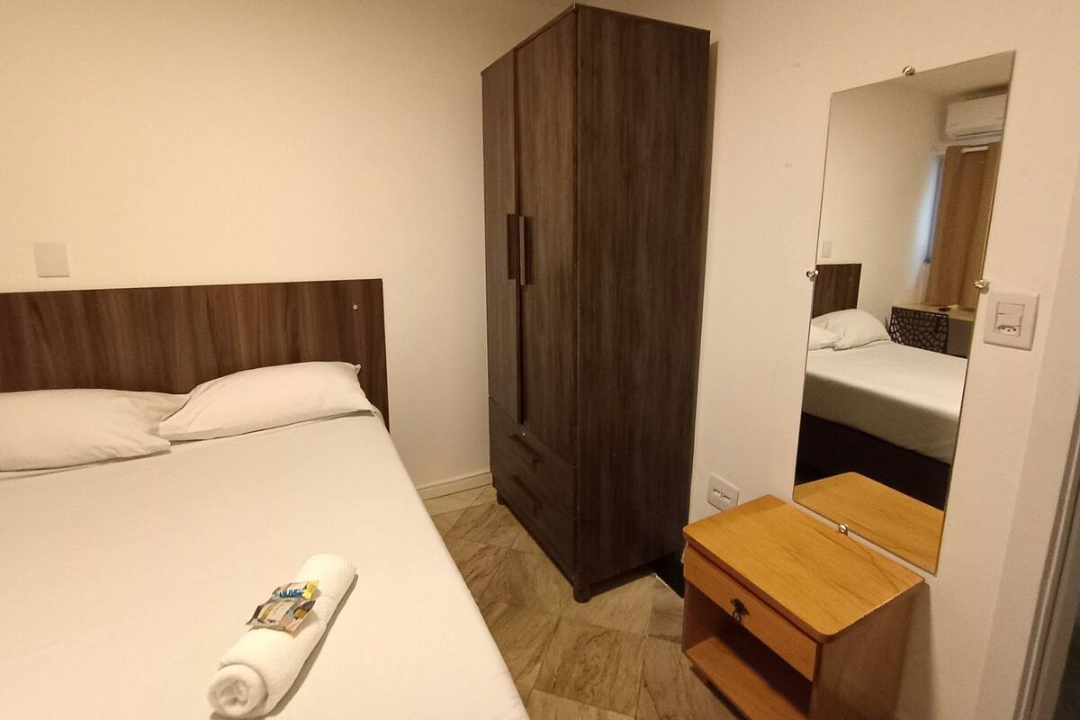 Ein Hotelzimmer mit Bett, Holzschrank, Nachttisch und Spiegel.