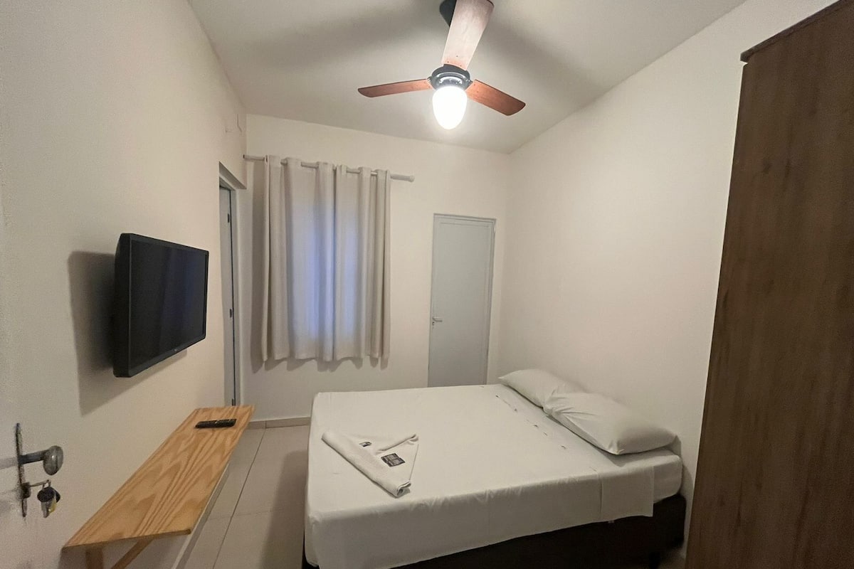 Ein Schlafzimmer mit einem Bett, einem an der Wand montierten Fernseher, einem Deckenventilator und einer Holzbank.