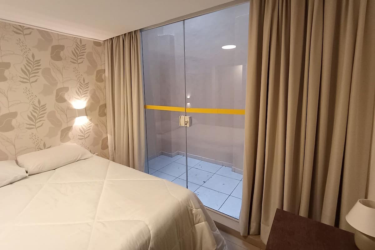 Ein Hotelzimmer mit Bett, einer Schiebetür zu einem Balkon und einer Wand mit Blattmuster.