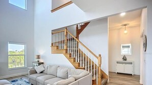 A spacious living room with a large L-shaped sectional sofa, a wooden staircase, and a small white cabinet.