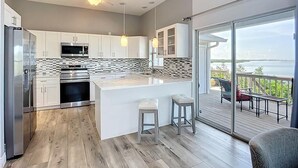 A modern kitchen with a central island, stainless steel appliances, and a large sliding glass door leading to a balcony with a view.