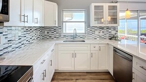 A modern kitchen with white cabinets, a tiled backsplash, a built-in oven, and a view of the outdoors.