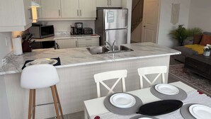 Cocina moderna con una isla central, electrodomésticos de acero inoxidable y comedor con sillas blancas y una mesa dispuesta para cuatro.