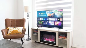 Una sala de estar con televisor de pantalla plana sobre un mueble de madera, un sillón de cuero marrón y una estantería.