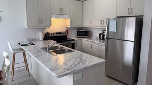 Una cocina moderna con armarios blancos, un refrigerador de acero inoxidable, un microondas y una estufa.