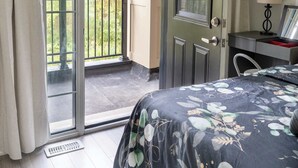 Un dormitorio con cama, escritorio, silla y puerta que da a un balcón.