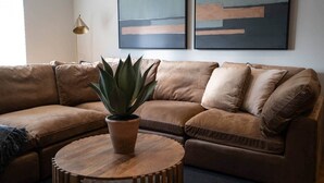 A brown leather sectional sofa with a round wooden coffee table and a potted plant. - Church Road Retreats - The Reef (Kessingland)