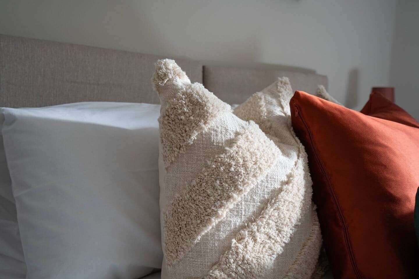 A bed with white and beige pillows, a brown pillow, and a wooden headboard.