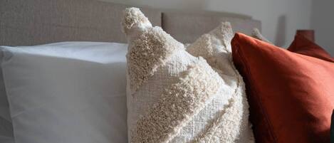 A bed with white and beige pillows, a brown pillow, and a wooden headboard.
