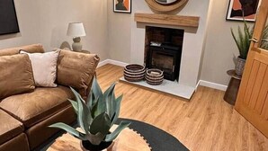A cozy living room with a brown leather sofa, a round wooden coffee table with a plant, a fireplace, and a large mirror on the wall. - Church Road Retreats - The Reef (Kessingland)