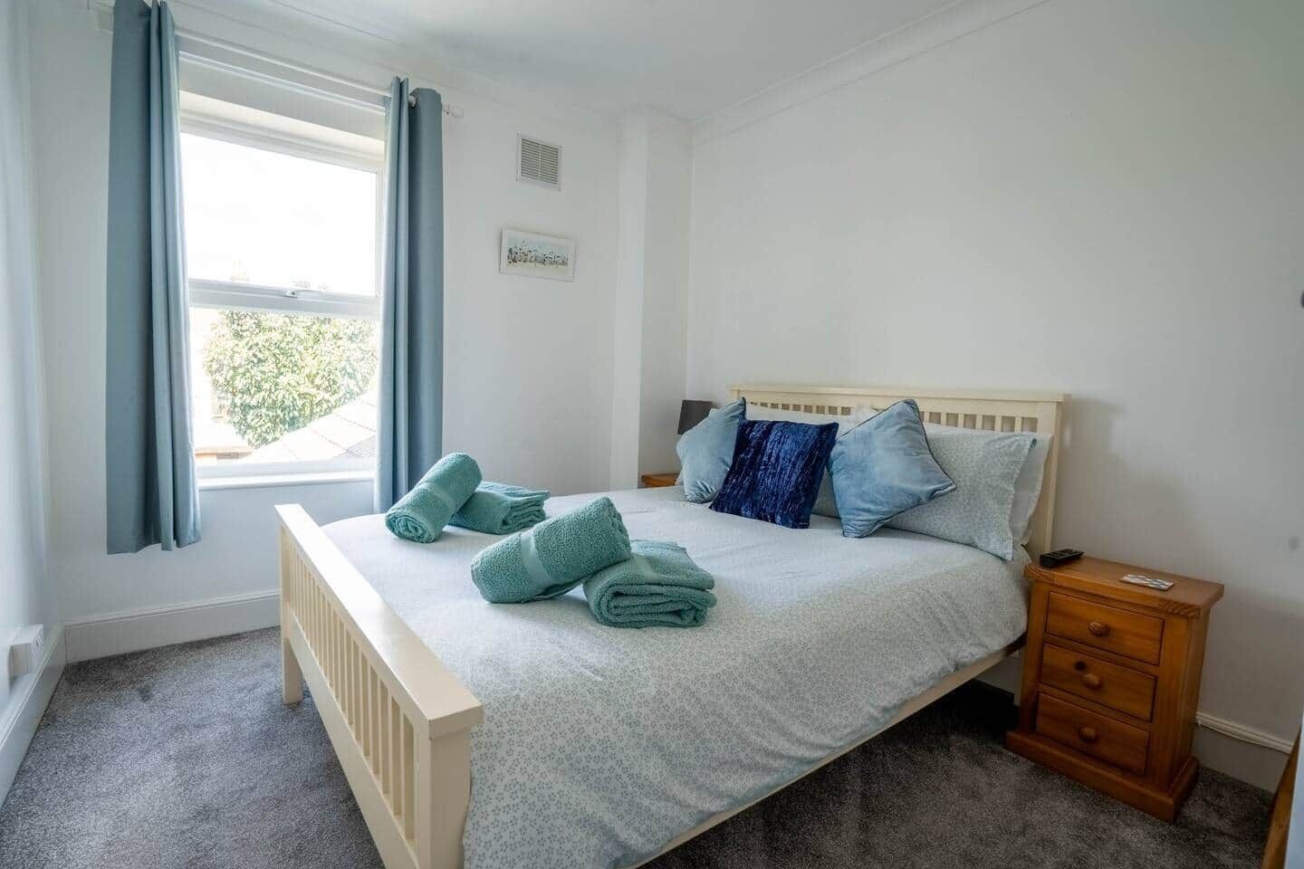 Ein Schlafzimmer mit Bett, Kissen, einem Nachttisch und einem Fenster mit Vorhängen.