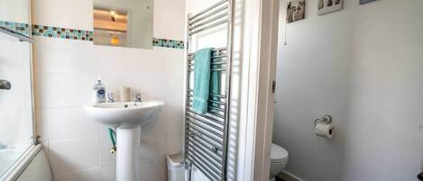 A bathroom with a white sink, a mirror, a towel rack, a toilet, and a shower area.