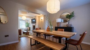 A dining area with a wooden table, benches, and chairs. There is a television mounted on the wall and a plant on the table.