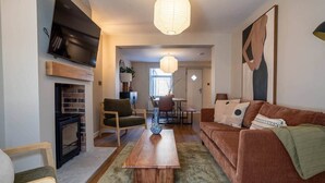 A living room with a fireplace, a sofa, a coffee table, and a dining area in the background.