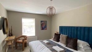 A bedroom with a large bed, a desk, a chair, a radiator, a window, and a ceiling light.