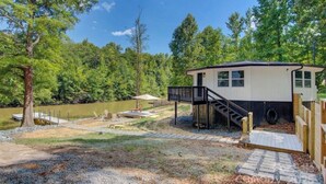 A cabin with a deck, a dock, and a small outdoor seating area by a lake.
