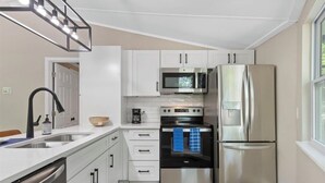 A modern kitchen with white cabinets, stainless steel appliances, a black faucet, and a window providing natural light.
