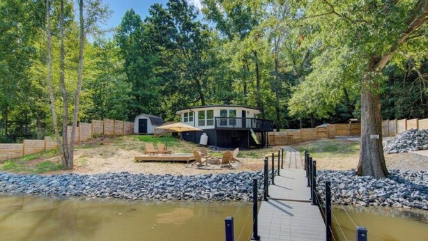 A lakeside cabin with a deck, outdoor seating, and a dock.