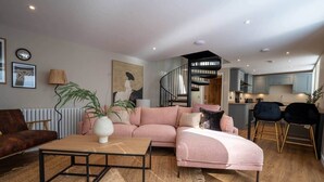 A modern living room with a pink sofa, a wooden coffee table, and a staircase leading to a kitchen. - Church Road Retreats - Coral Cottage (Kessingland)