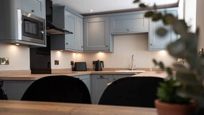A modern kitchen with grey cabinets, a built-in microwave, and a sink. - Church Road Retreats - Coral Cottage (Kessingland)
