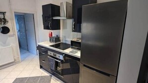 A modern kitchen with black cabinets, a stainless steel refrigerator, and a tiled floor.