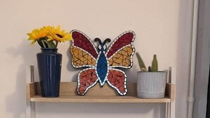 A shelf with a mosaic butterfly, a vase with sunflowers, a cactus, a digital thermometer, and a marble tray.