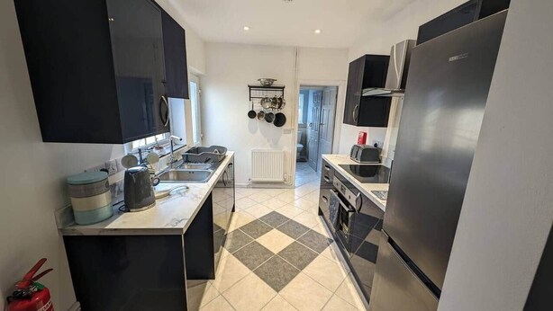A modern kitchen with black cabinets, stainless steel appliances, and a tiled floor.