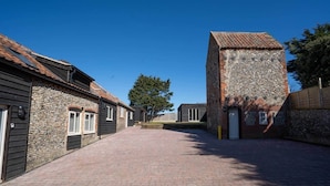 A courtyard with stone buildings, a paved walkway, and a clear blue sky. - Church Road Retreats - The Cove (Kessingland)