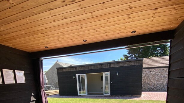 Een jacuzzi met houten plafond en uitzicht op een gebouw op de achtergrond.