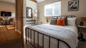 Een slaapkamer met een bed, nachtkastjes, een raam met zonwering, een schilderij, en een zithoek met stoelen en een tafel.