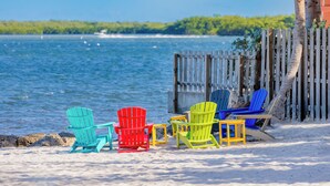Een strand met kleurrijke Adirondack stoelen en een houten hek.