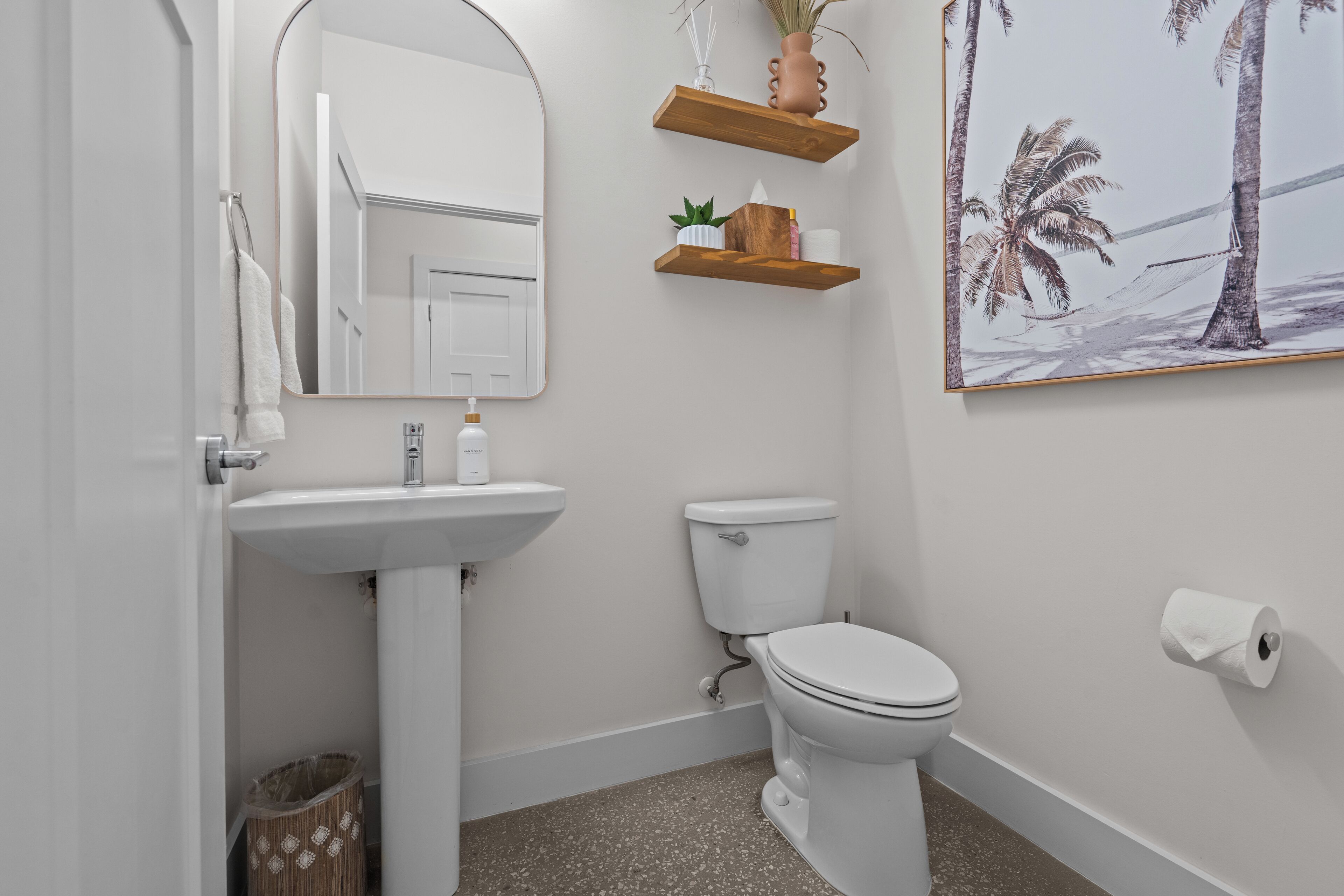 A bathroom with a white sink, toilet, and a framed picture of palm trees.