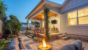 Eine Terrasse mit Feuerstelle, Sitzgelegenheiten im Freien und einem überdachten Bereich mit Deckenventilator.
