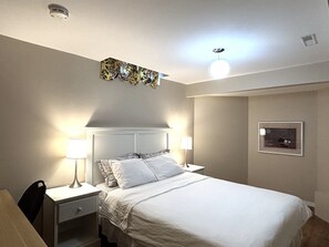 Une chambre à coucher bien rangée, avec un lit, deux tables de chevet dotées de lampes, un luminaire au plafond et un élément décoratif mural.