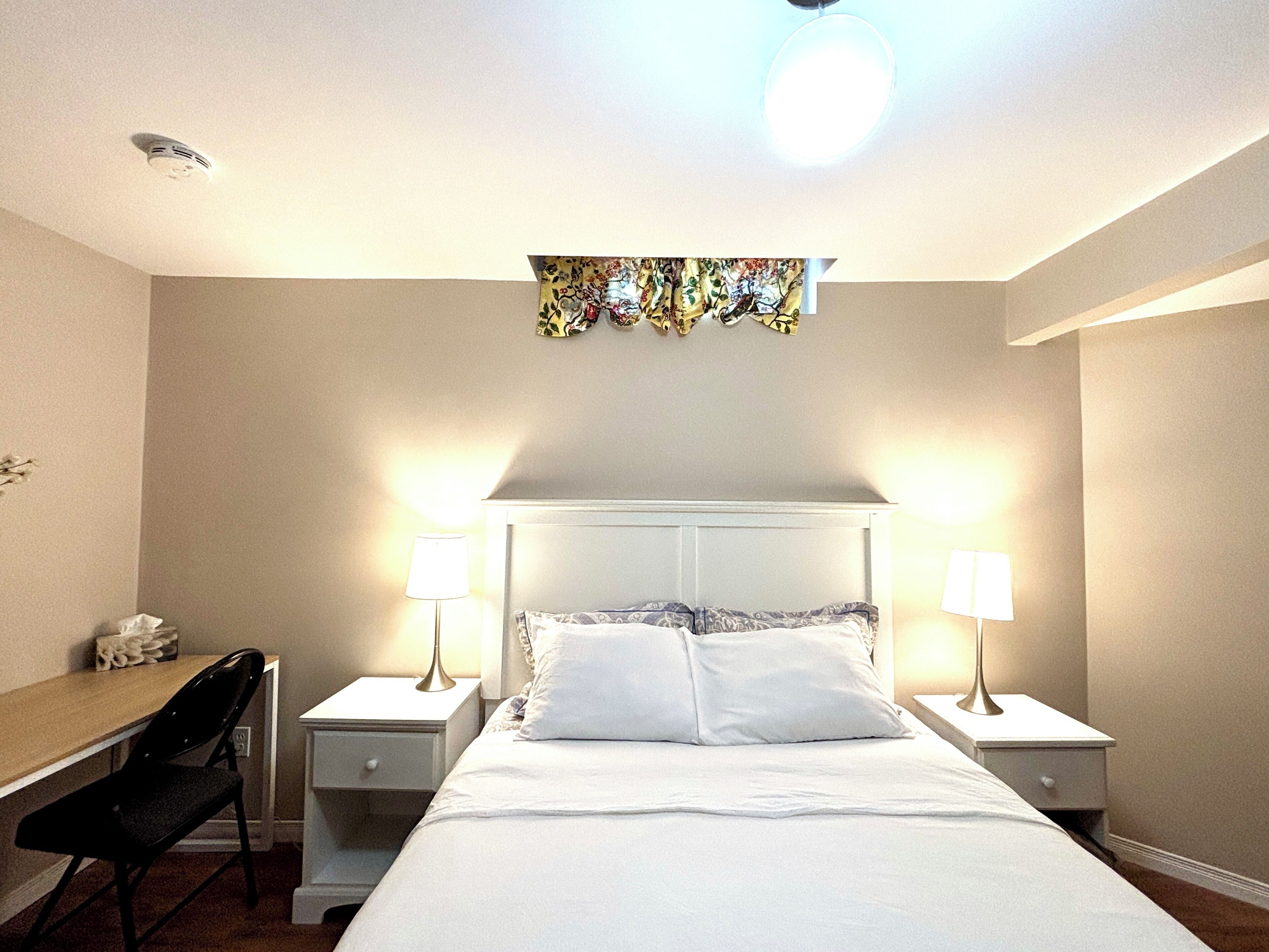 A hotel room with a bed, two bedside lamps, a desk, and a chair.