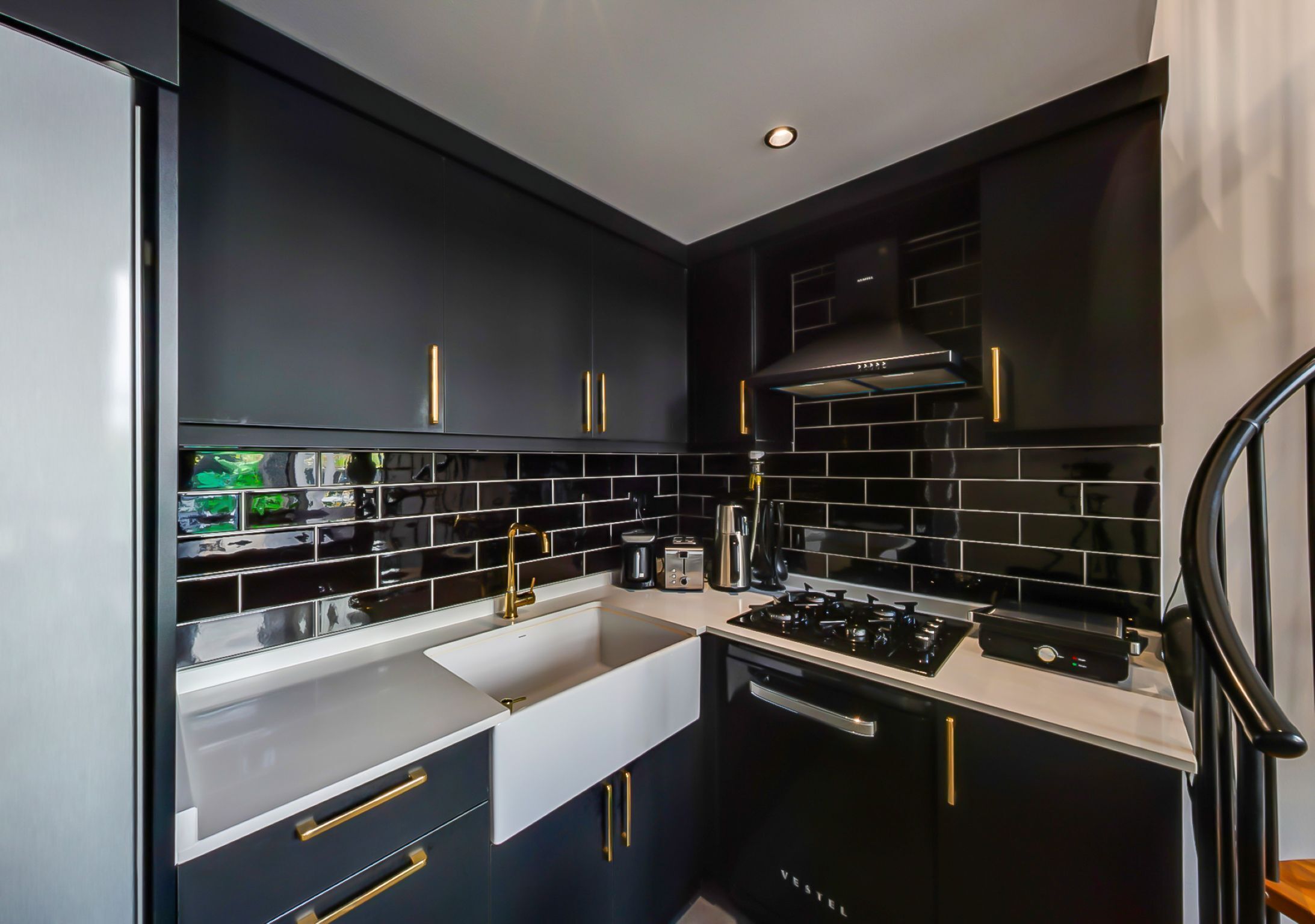 A modern kitchen with black cabinetry, white countertops, and gold handles.
